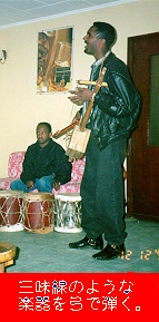 （写真）革ジャンの男が三味線のような楽器を弾きながら即興で歌う（写真）
