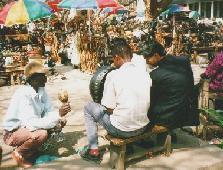 （写真）民族楽器を弾いている商人。となりには日本人観光客が座っている（写真）